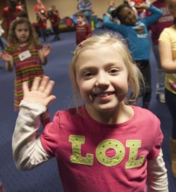 girl smiling and waving as kids move in the background